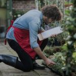 Side view of male gardener with clipboard working outside greenhouse